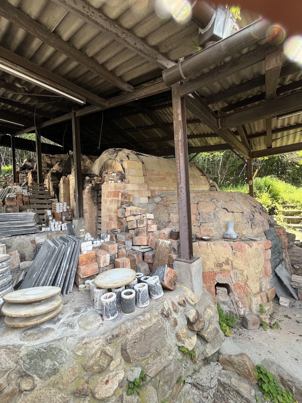 萩市の伝統的な登り窯（のぼりがま）の全体像。赤レンガと土で構築された歴史的な窯で、萩焼の焼成に使用されている。金属製の屋根に覆われた施設内に、製作工程で使用される道具や材料が配置されている